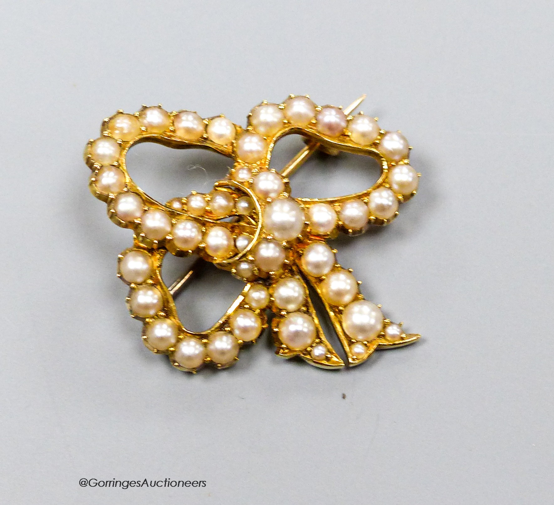 A yellow metal and split pearl set ribbon bow brooch, 30mm, gross weight 6.1 grams.